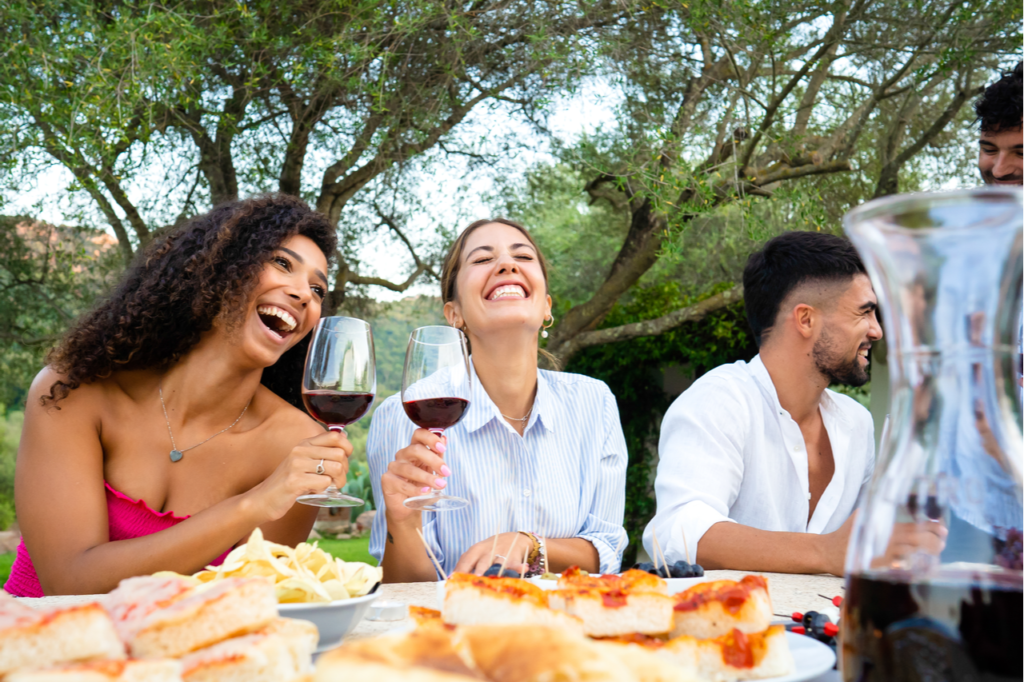 Mixed group of young happy friends celebrating outdoor with snacks and alcoholic drinks.