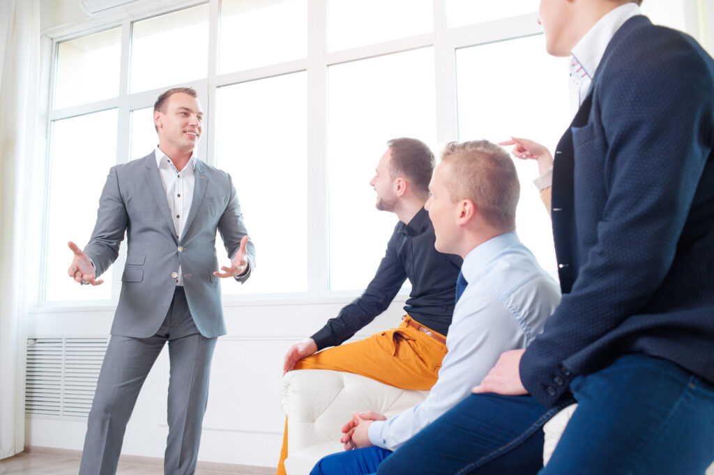 Man in grey suit talking to his colleagues.