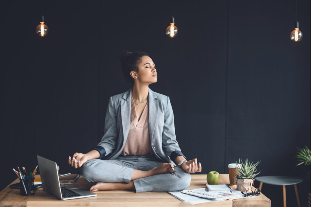 Businesswoman sitting in lotus pose on table while meditating in office.