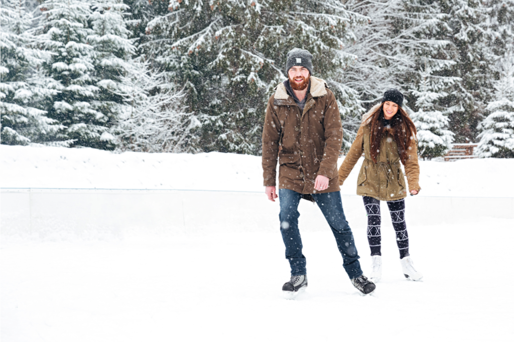 Smiling young couple ice skating outdoors with snow on background.