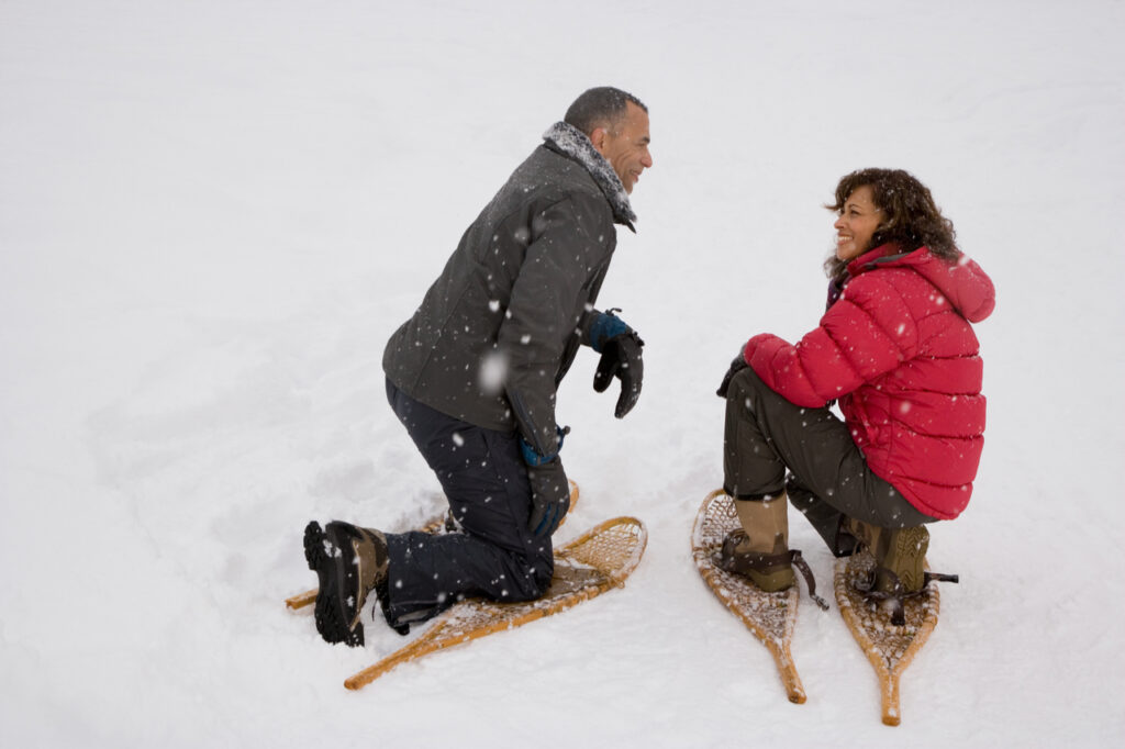 Couple crouching in the snow wearing snowshoes as a snow sports.