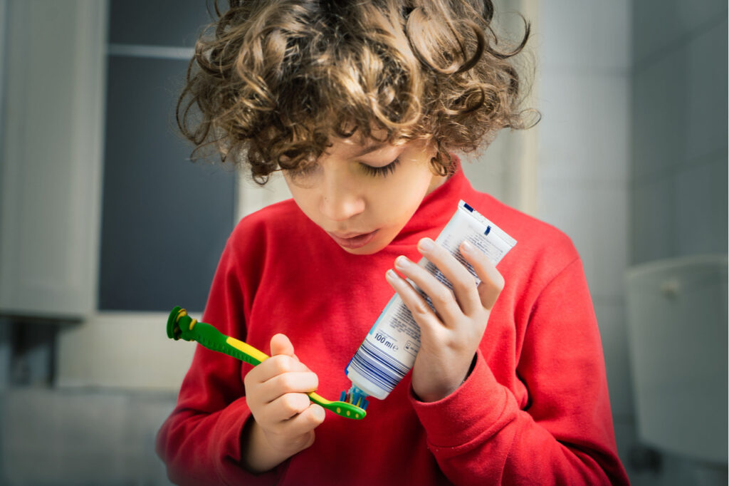 Child puts toothpaste on the toothbrush.