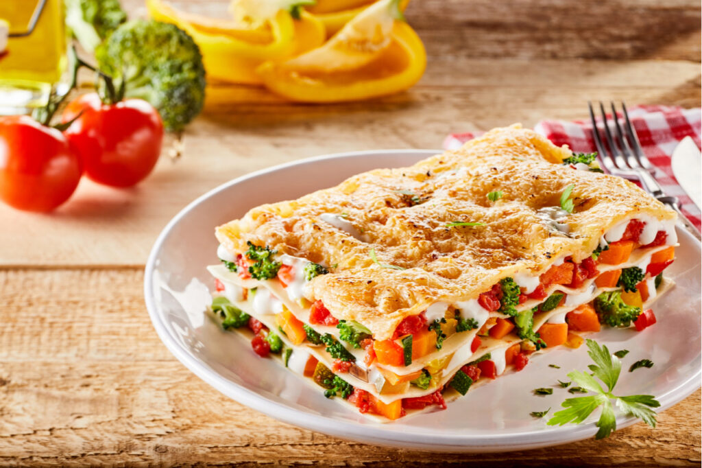 Single portion serving of a colorful appetizer of Italian vegetable lasagna made with assorted fresh veggies, melted mozzarella and pasta sheets on a rustic table.