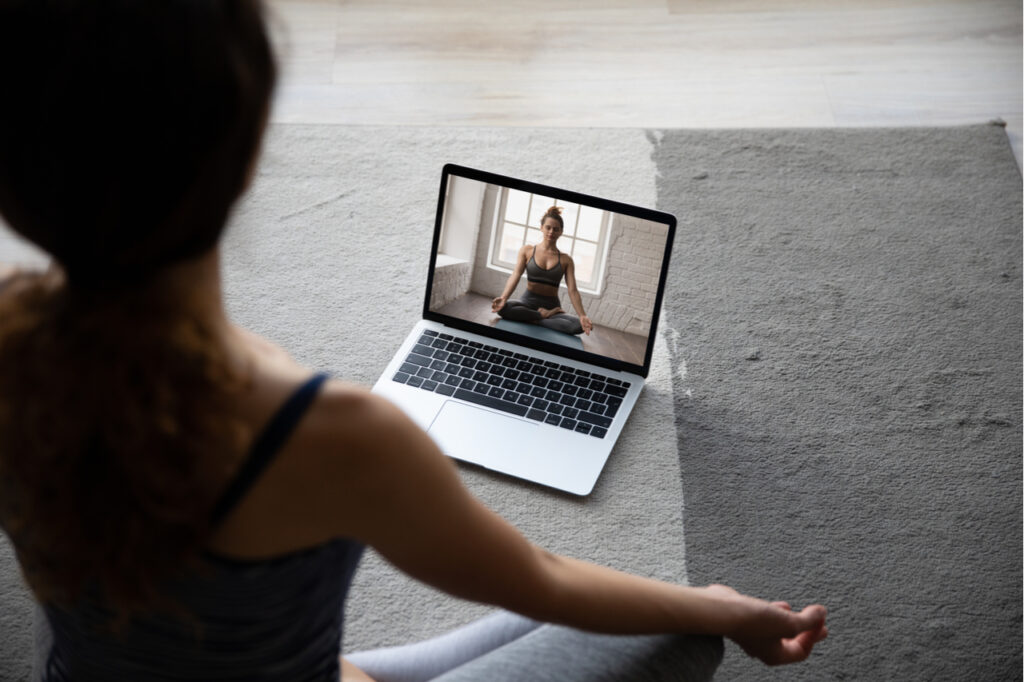 Back view of fit sporty woman sit on floor at home mediate practice yoga having video call with coach.