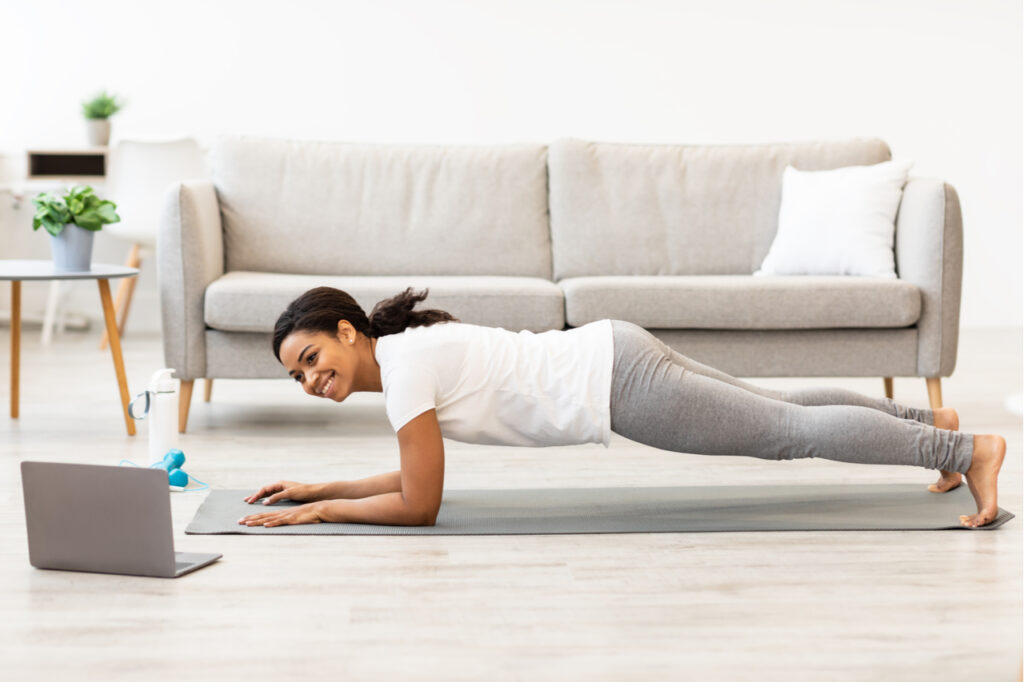 Woman exercising at home while watching an online tutorial as one of the fitness trends.