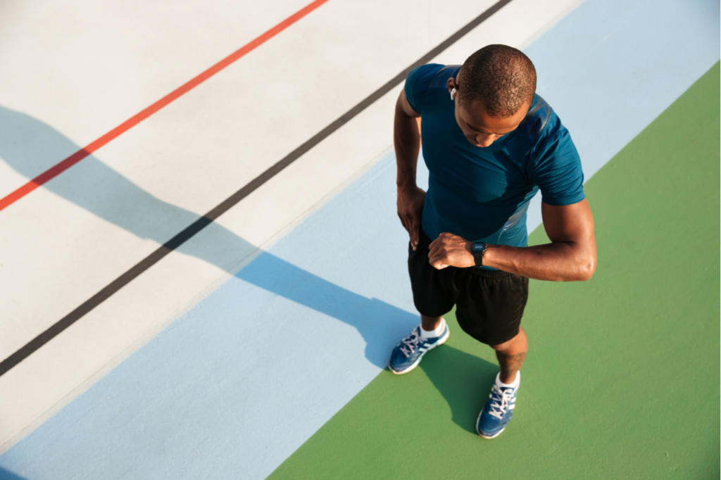 Top view of a young sportsman looking at his whoop band while standing on a track field.