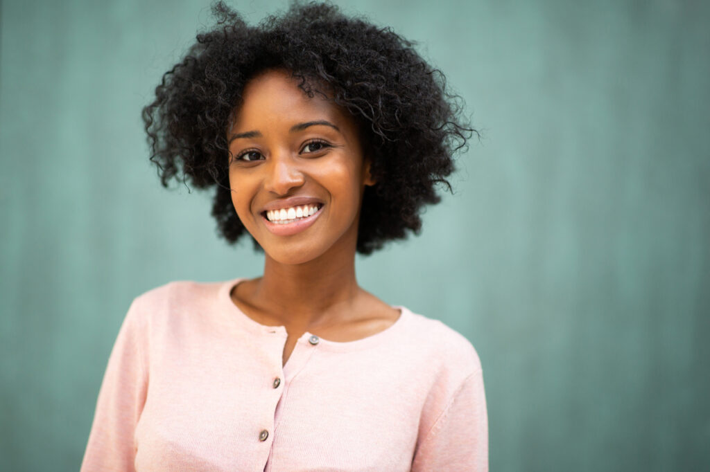 Close up portrait beautiful young black woman smiling against green background.