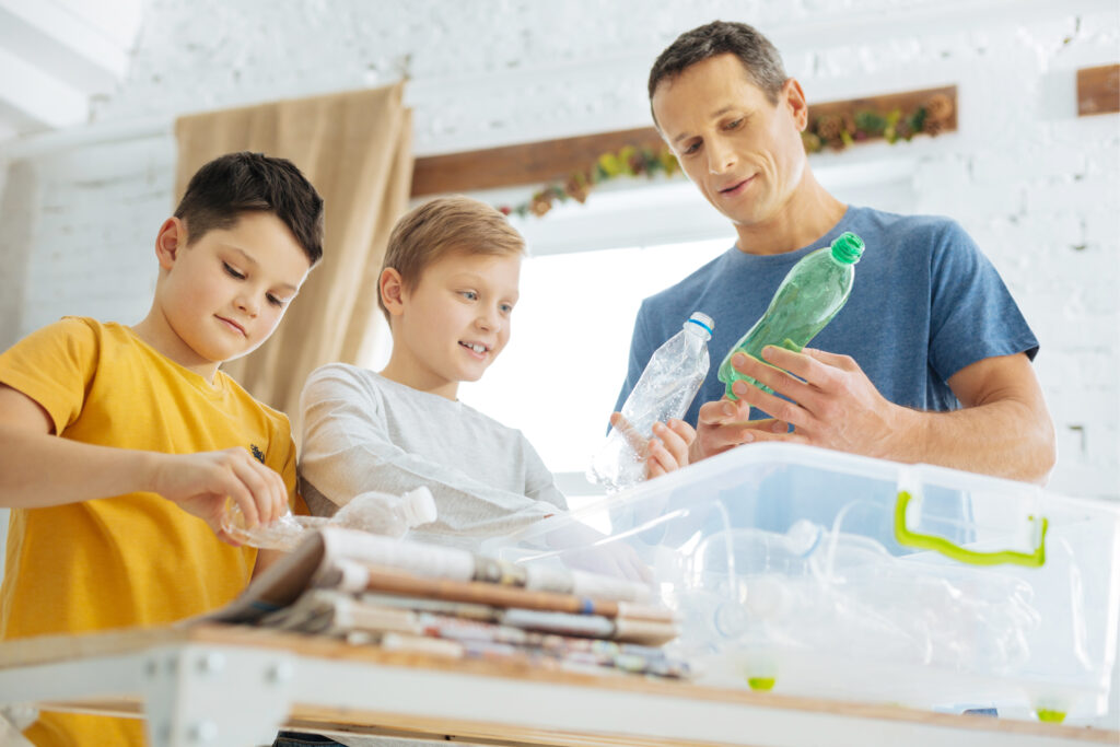Caring about nature. Charming young man and his pre-teen sons preparing plastic bottles for recycling, crushing the bottles and putting them into special containers
