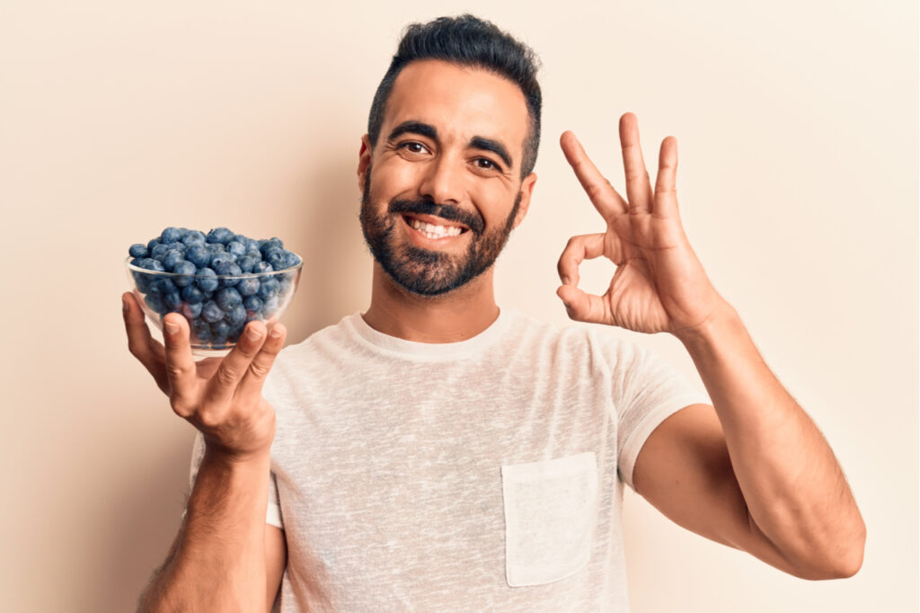 Man holding blueberries doing ok sign with fingers.