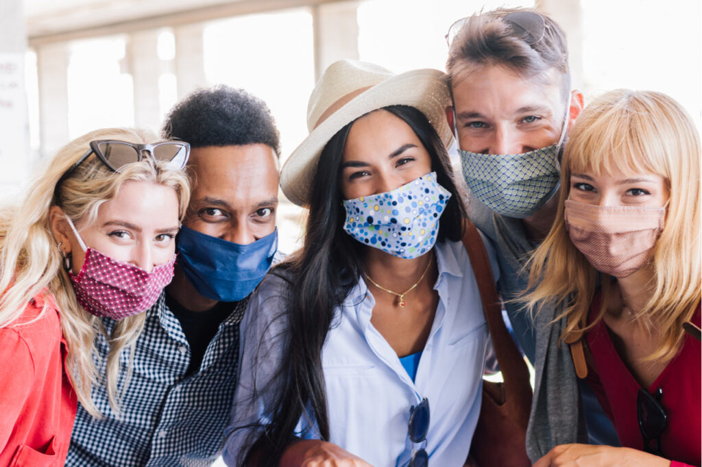 Group of young happy friends wearing face mask during Covid pandemic smiling at the camera.