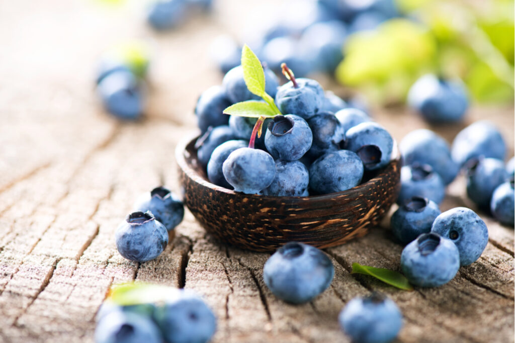 Juicy and fresh blueberries with green leaves on rustic table.