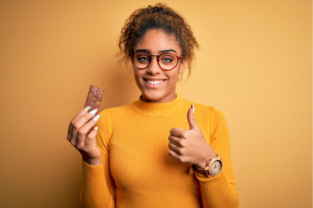 Woman eating IQ bar with her thumbs up.