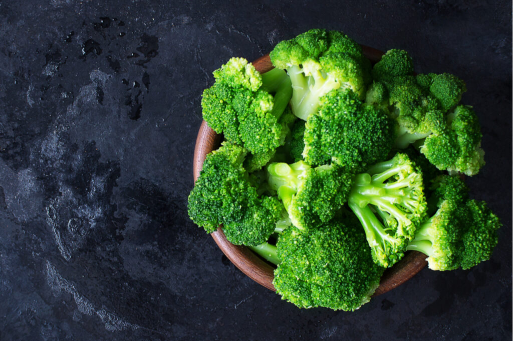 Fresh raw broccoli in a wooden bowl on a dark background.