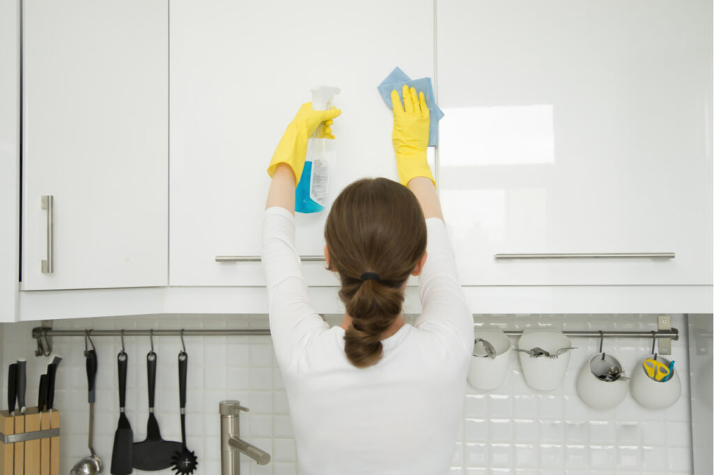 Woman cleaning a surface of white kitchen wall cabinet.