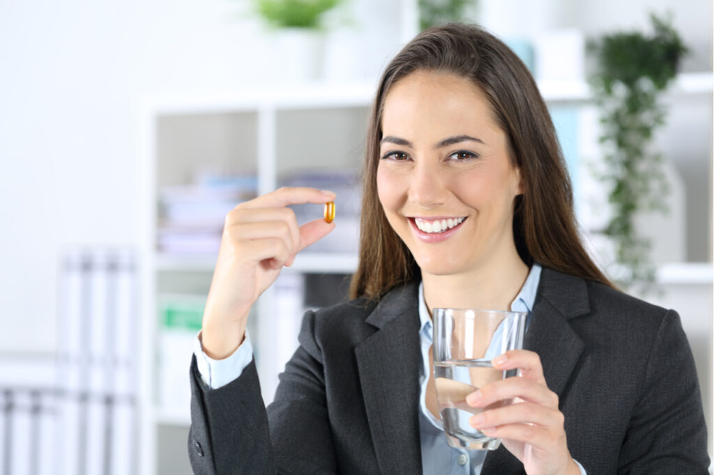 Woman shows vitamin pill and water glass at the office.