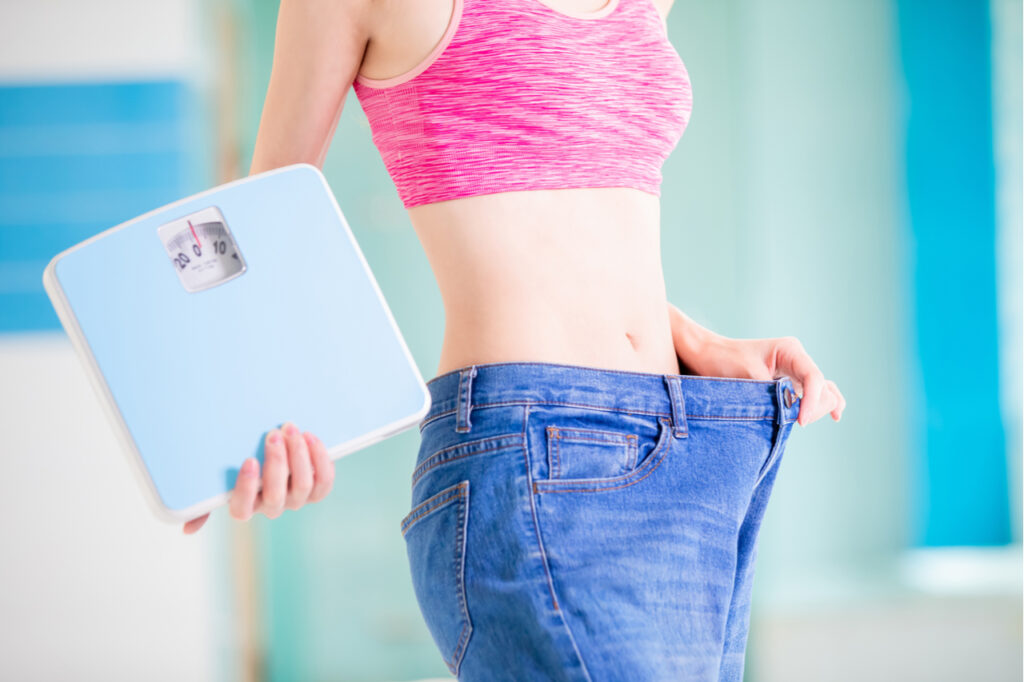 Woman holding jeans and bathroom scale.