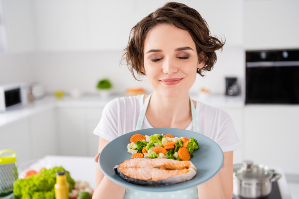 Close up photo of woman holding grilled salmon trout fillet steak with garnish as a types of diet.