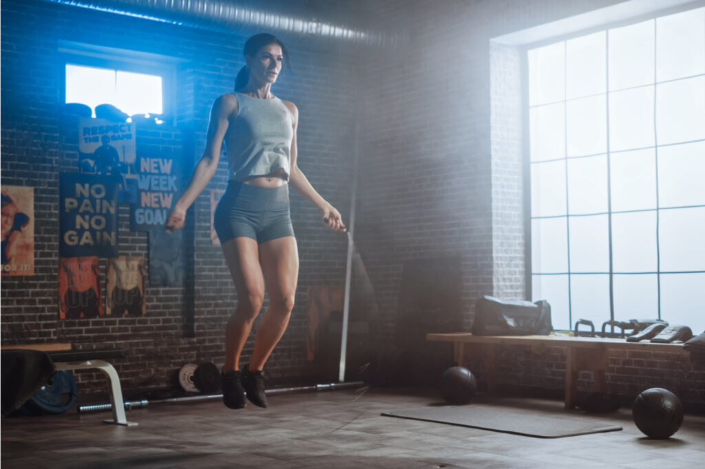 Woman working out using jumping rope with motivational posters in the background..