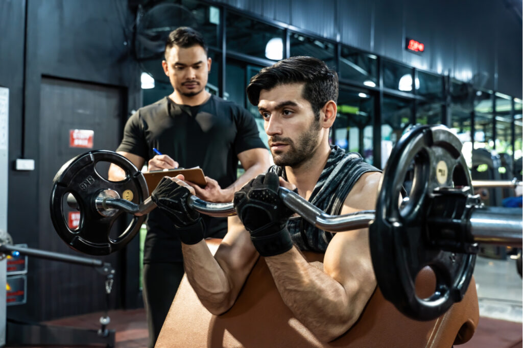 Man wearing workout gloves while practicing weight lifting exercise with professional sport coach.