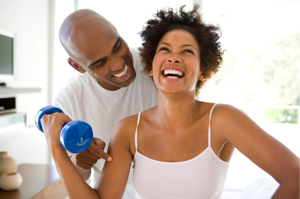 Man smiling at woman exercising with weights at home.