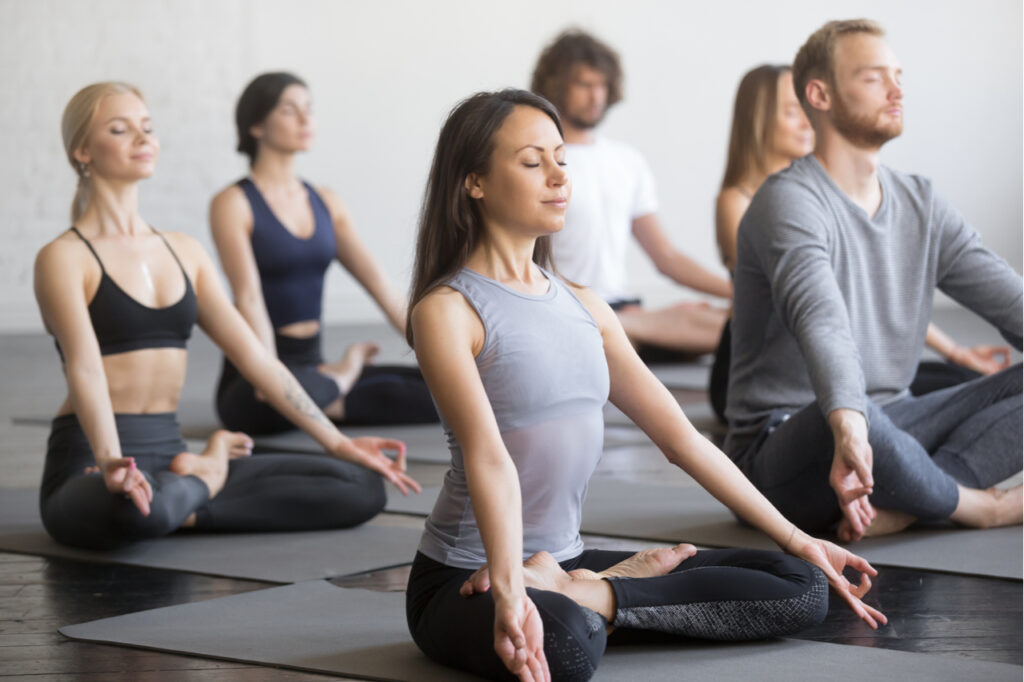 Group of young sporty people practicing yoga lesson with instructor.