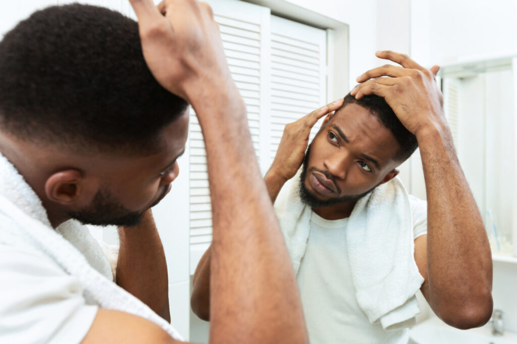 Man checking for thinning hair in mirror at bathroom needing hims hers hair loss.