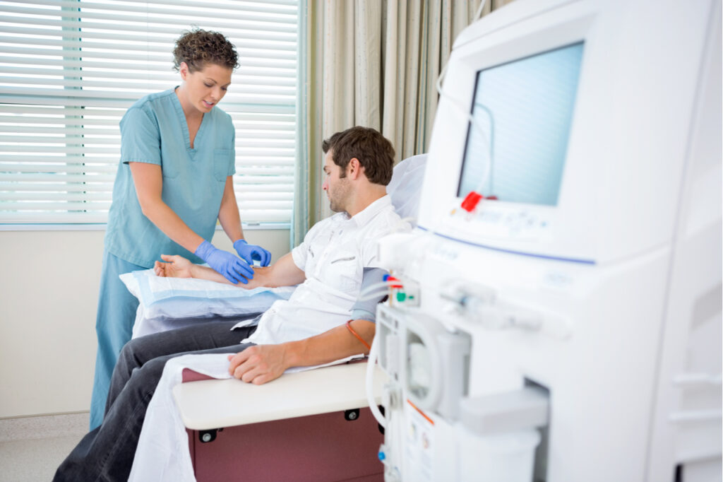Mid adult female nurse injecting patient for dialysis treatment in hospital room.