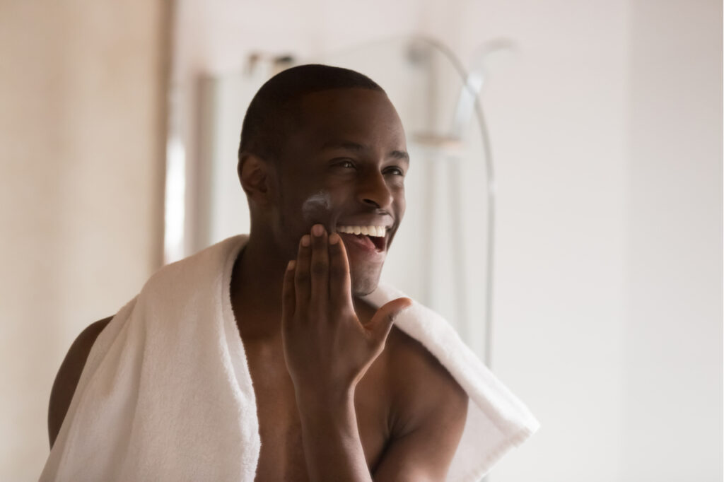 Man looking in mirror at bathroom applying moisturizer.