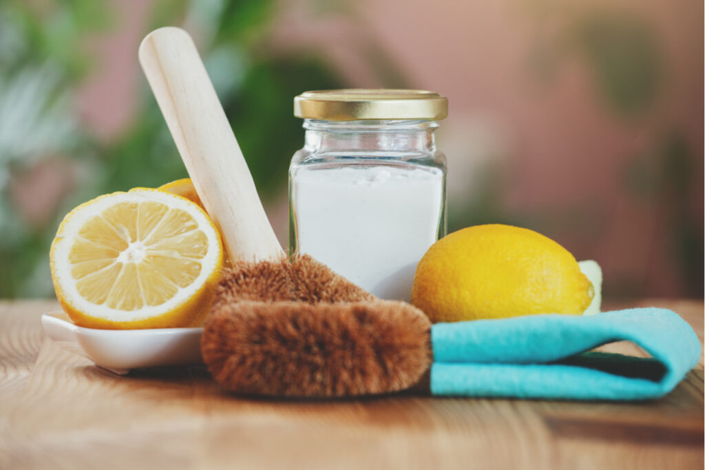 eco-friendly house cleaners, baking soda, lemon, bamboo cleaning brush and green cloth on wooden table, non toxic cleaning