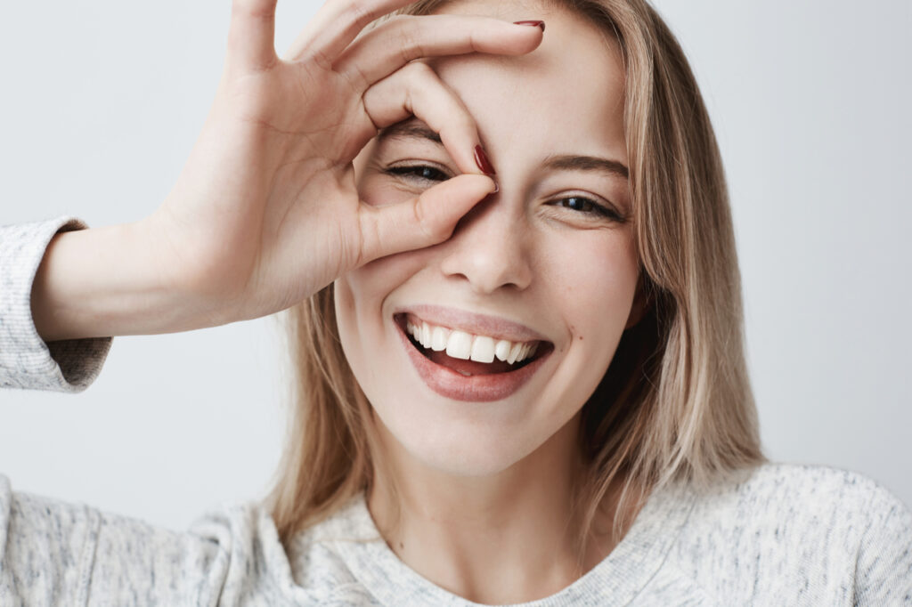 Woman looking at the camera smiling with her fingers in okay gesture.