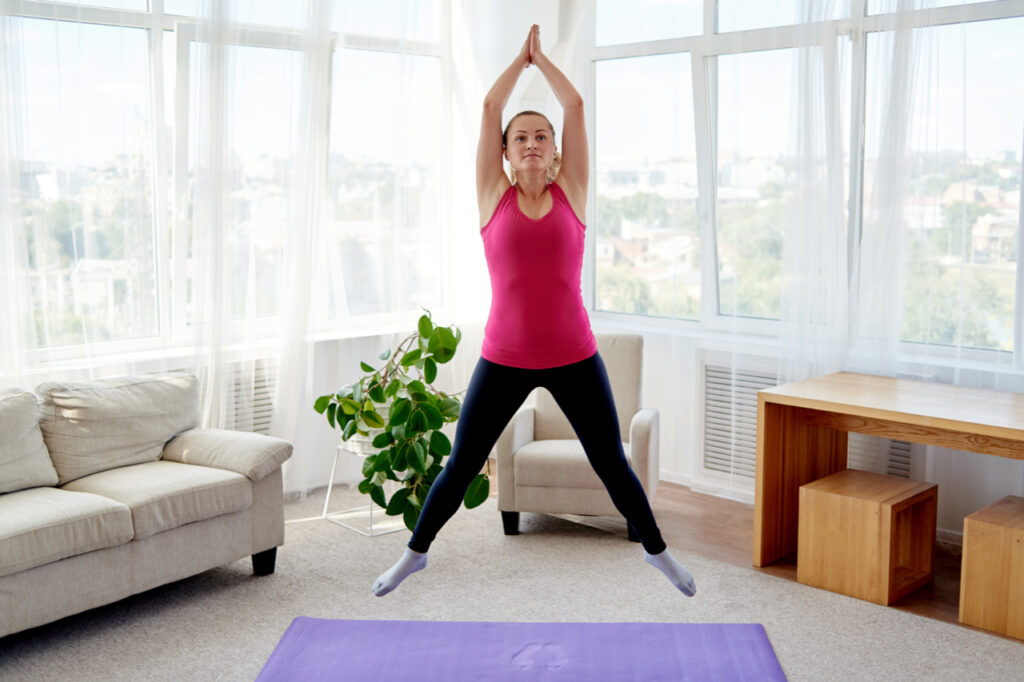 Young fitness woman doing jumping jacks or star jump exercise at home.
