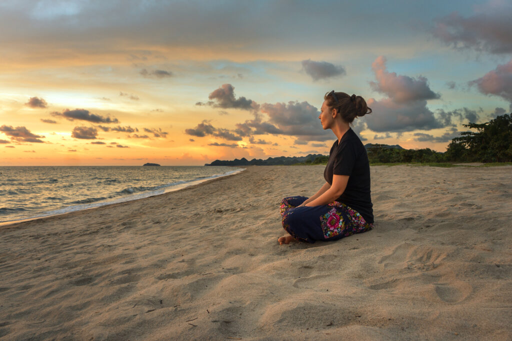 Woman sitting on beach sand and relaxing at sunset time.