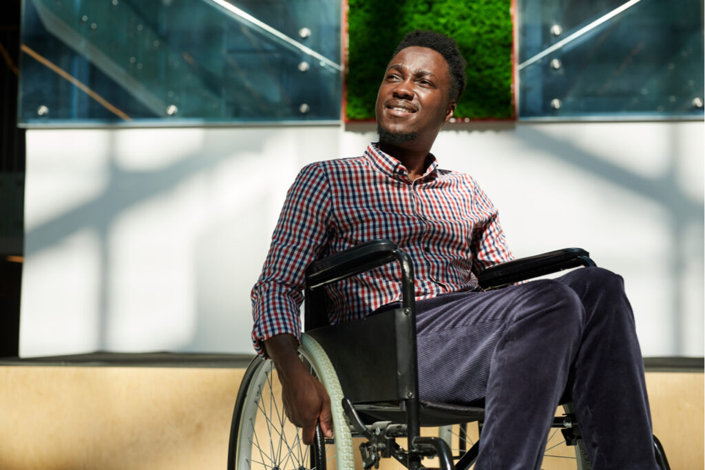 Man in wheelchair looking away and smiling at modern office.
