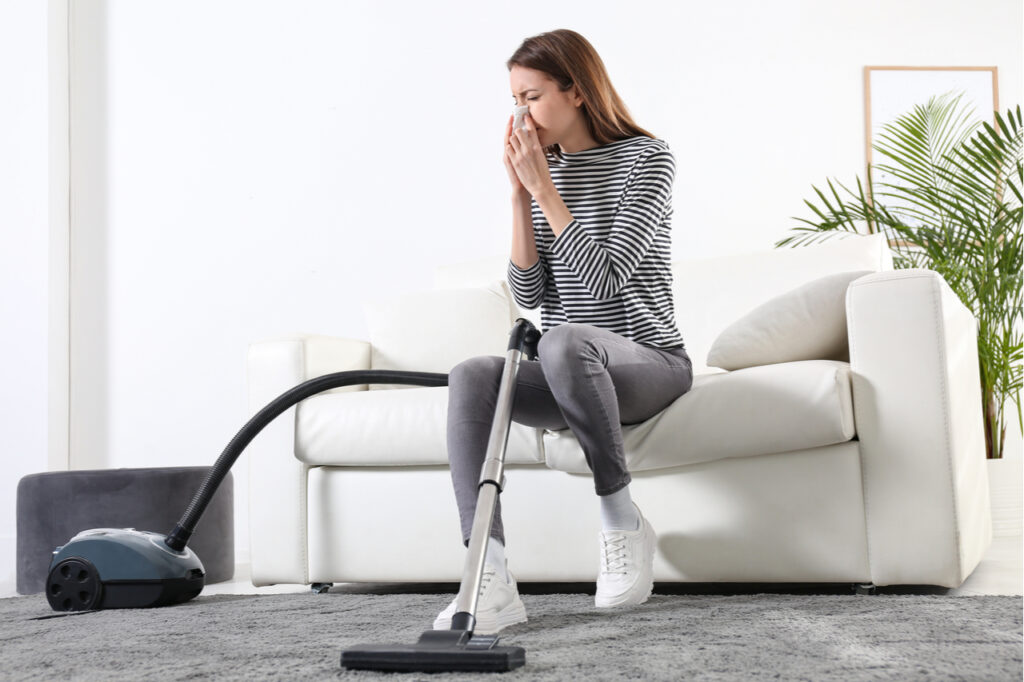 Woman suffering from dust allergy while vacuuming house that needs a healthy mind and body.