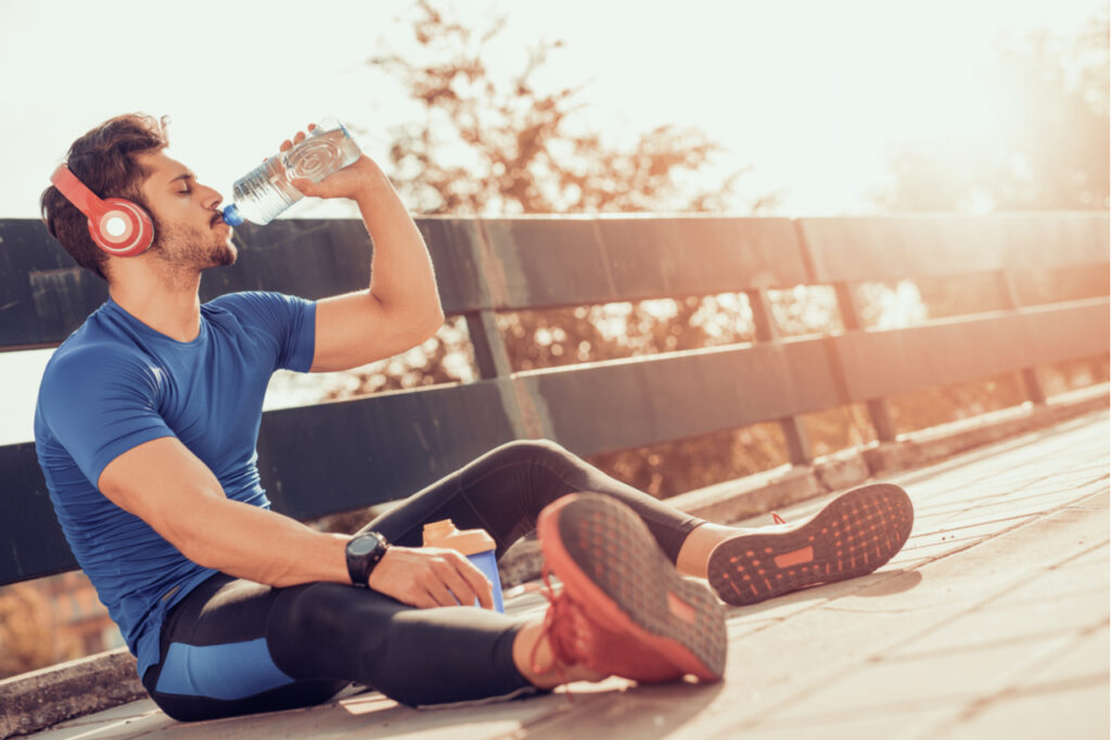 Man drinking some water from a bottle while sitting and resting after training.