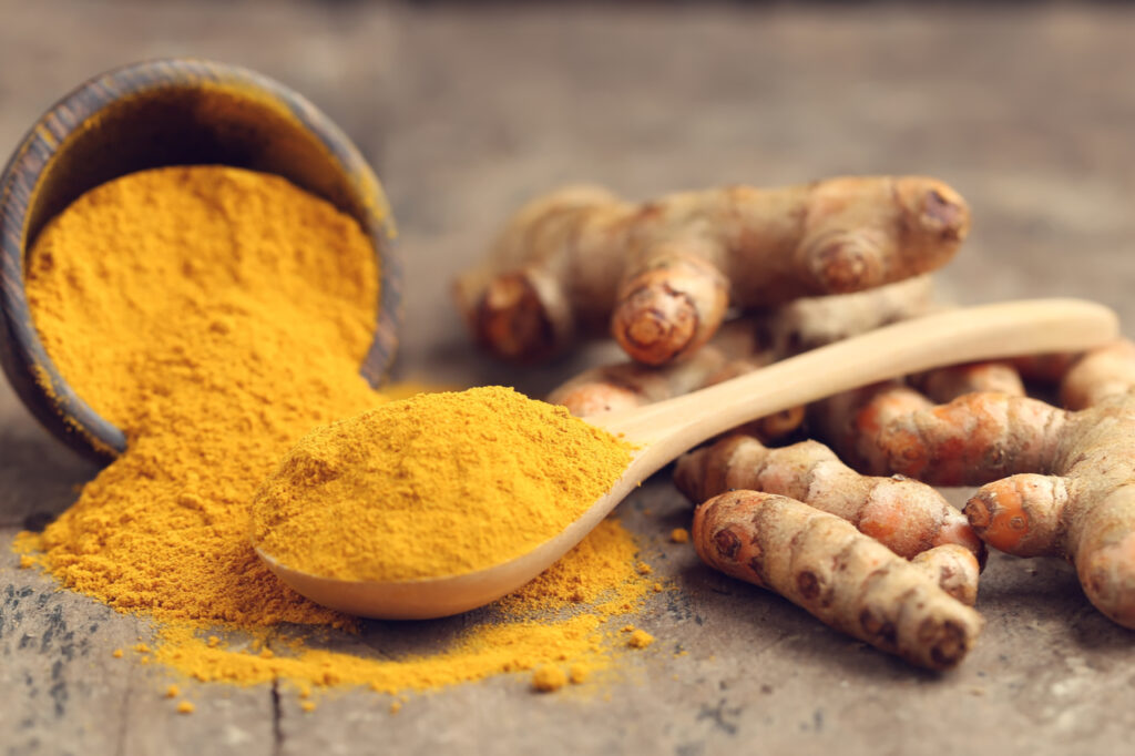 Turmeric powder and fresh turmeric on wooden background.