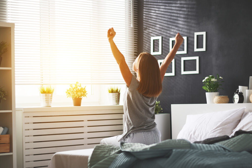 Young happy woman woke up in the morning in the bedroom by the window for international women's day.