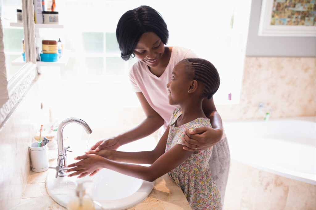 High angle view of mother and daughter washing hands at sink in bathroom.