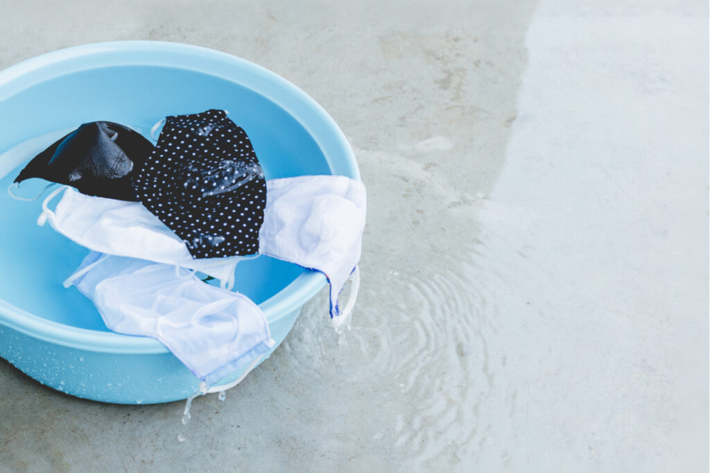 Fabric masks are soaked in blue plastic basin that water is overflowing ready for washing and rinse.
