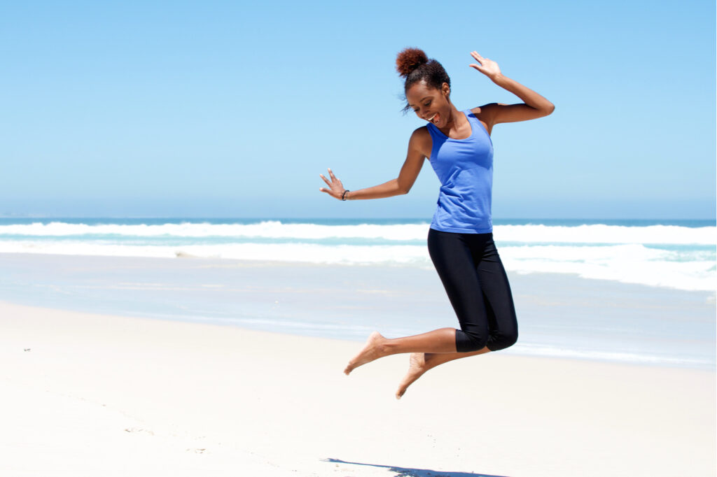 Sporty woman jumping full of energy at the beach.