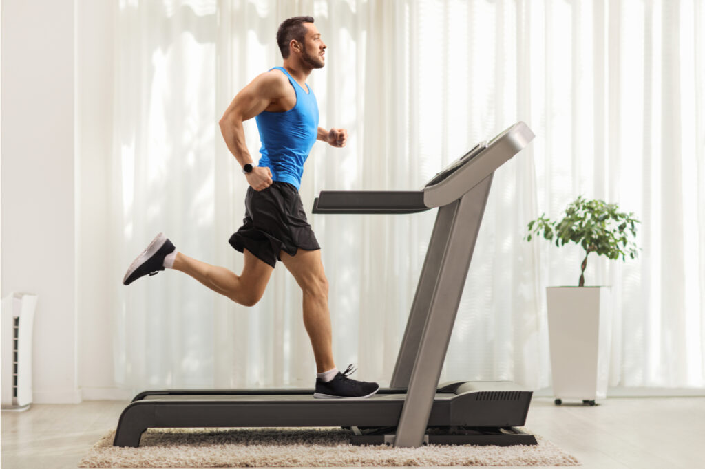 Full length profile shot of a young man running on a treadmill at home
