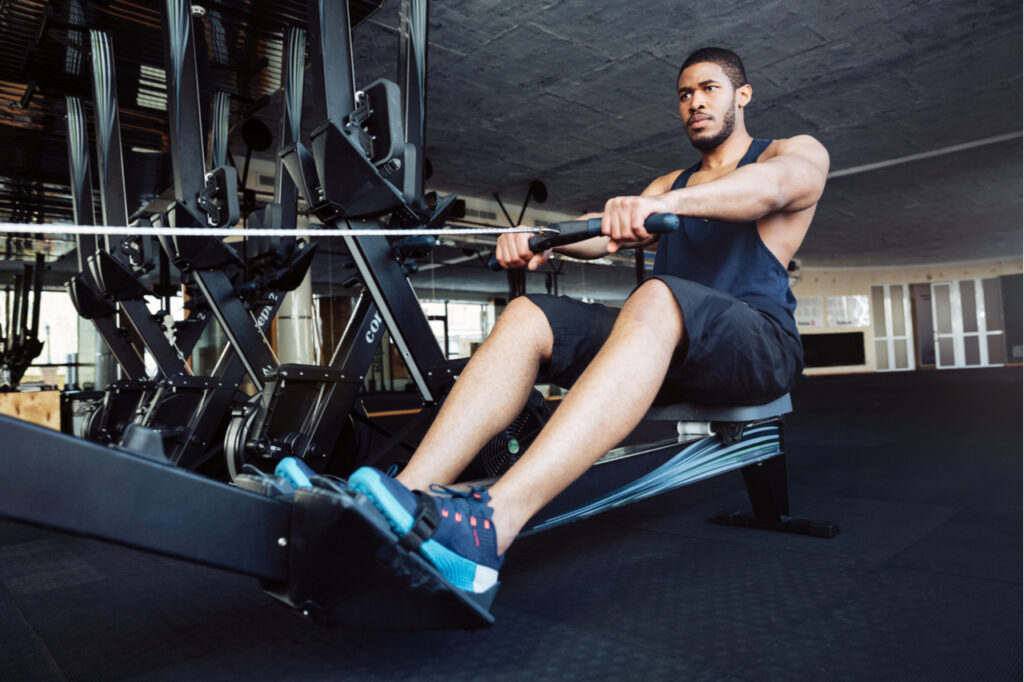 Muscular fit man using rowing machine at gym.