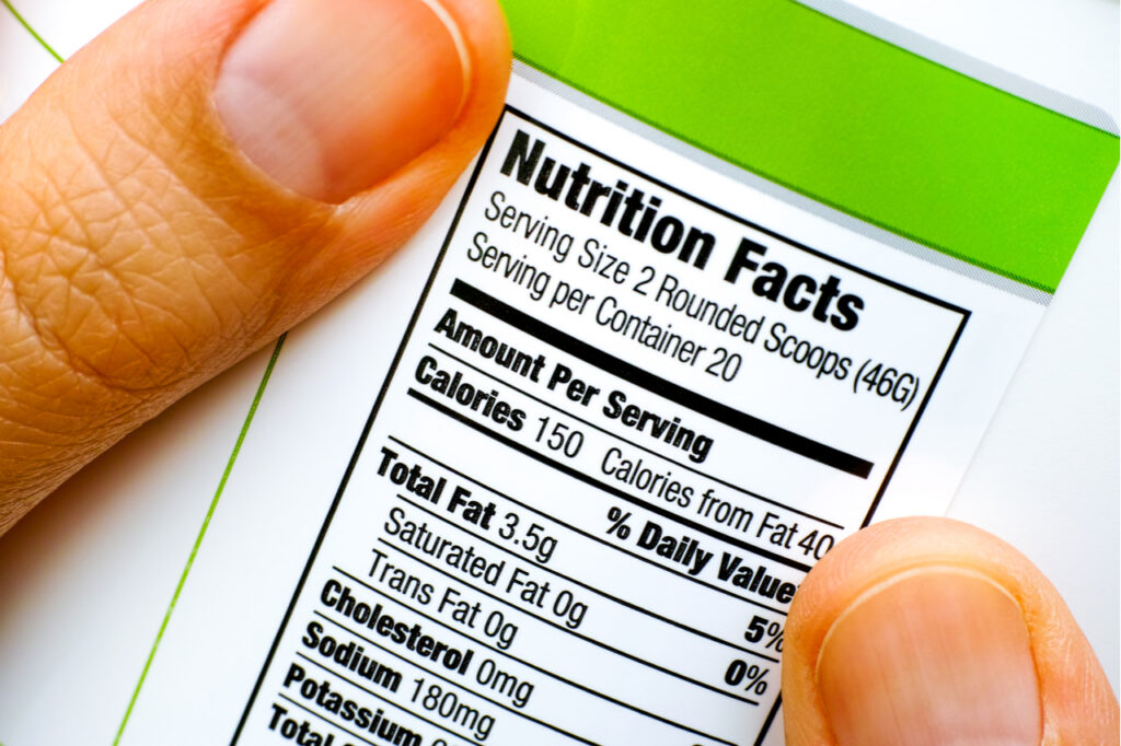 Woman fingers with protein jar. Reading nutrition label. Closeup.