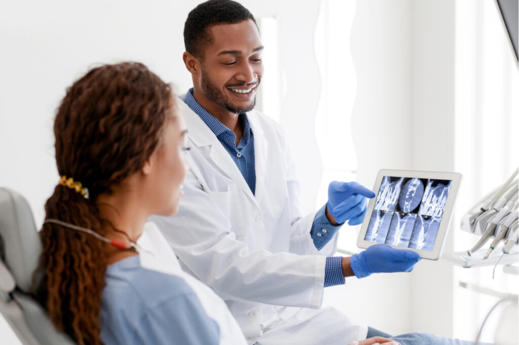 African American dentist and woman patient looking at x-ray picture on digital tablet at clinic