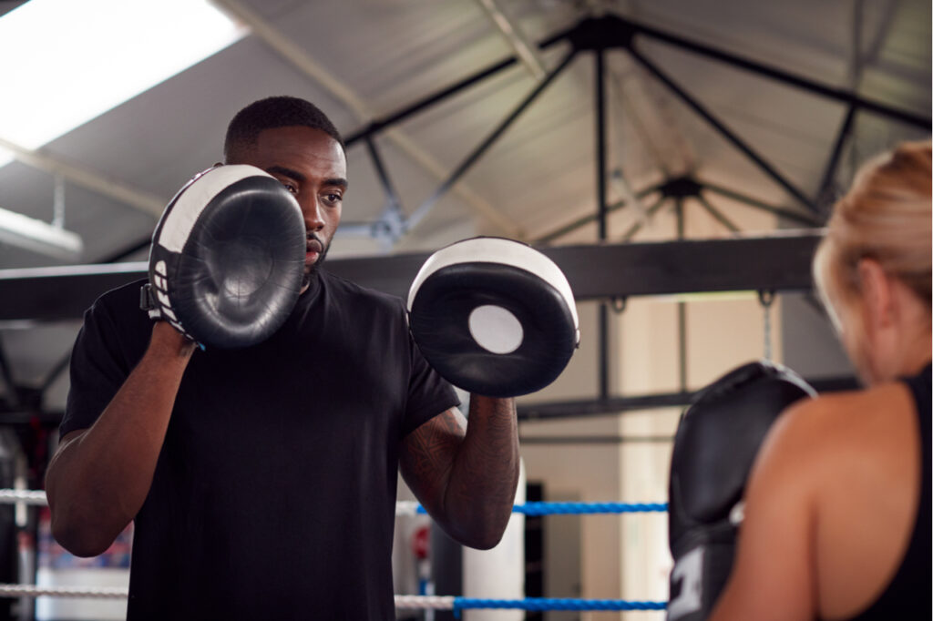 Male personal trainer sparring with female boxer in the gym.