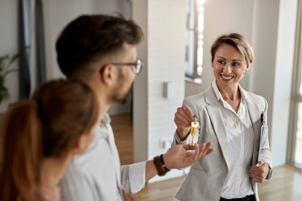 Agent giving new house key to a young couple that started a passive income plan by investing in real state.