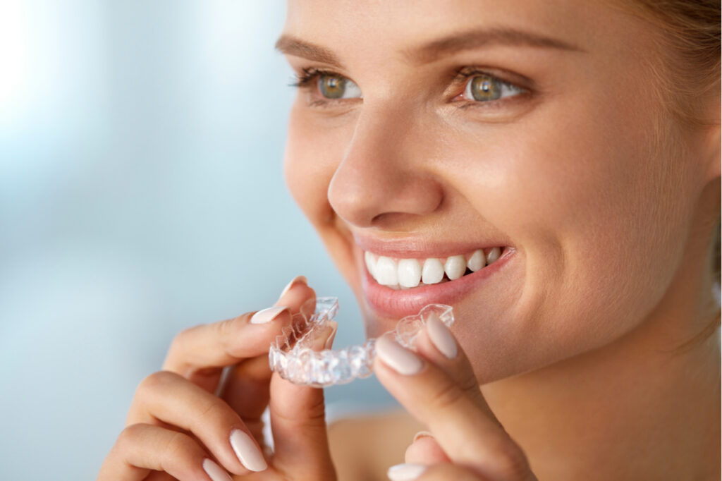 Image of young woman holding invisible braces, How to straighten your teeth at home.