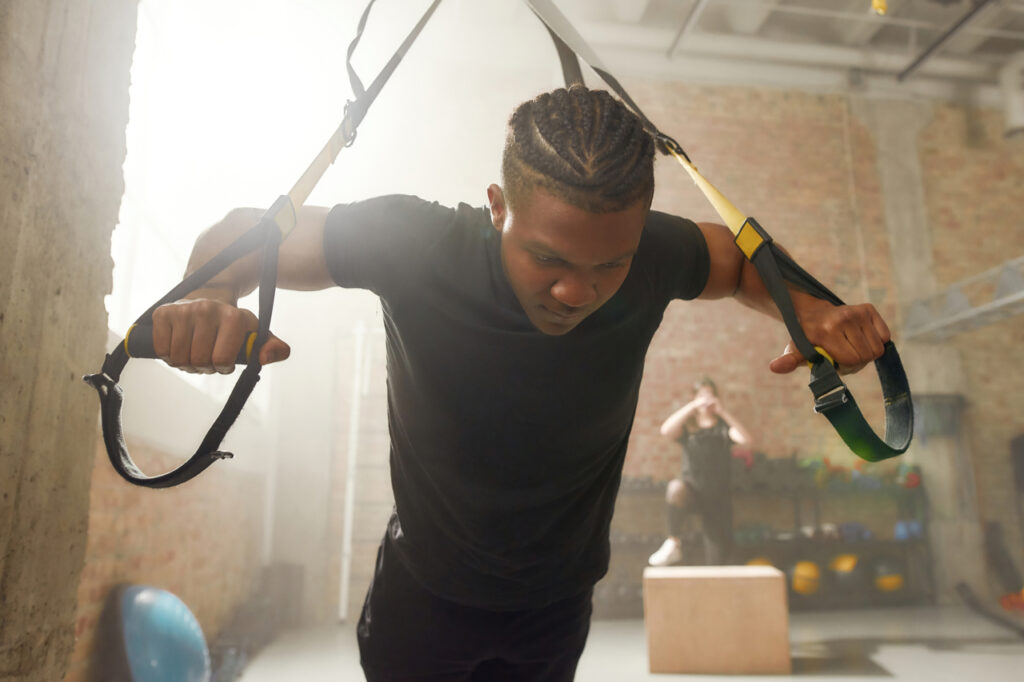 Athletic young man doing fitness TRX training exercises at industrial gym.