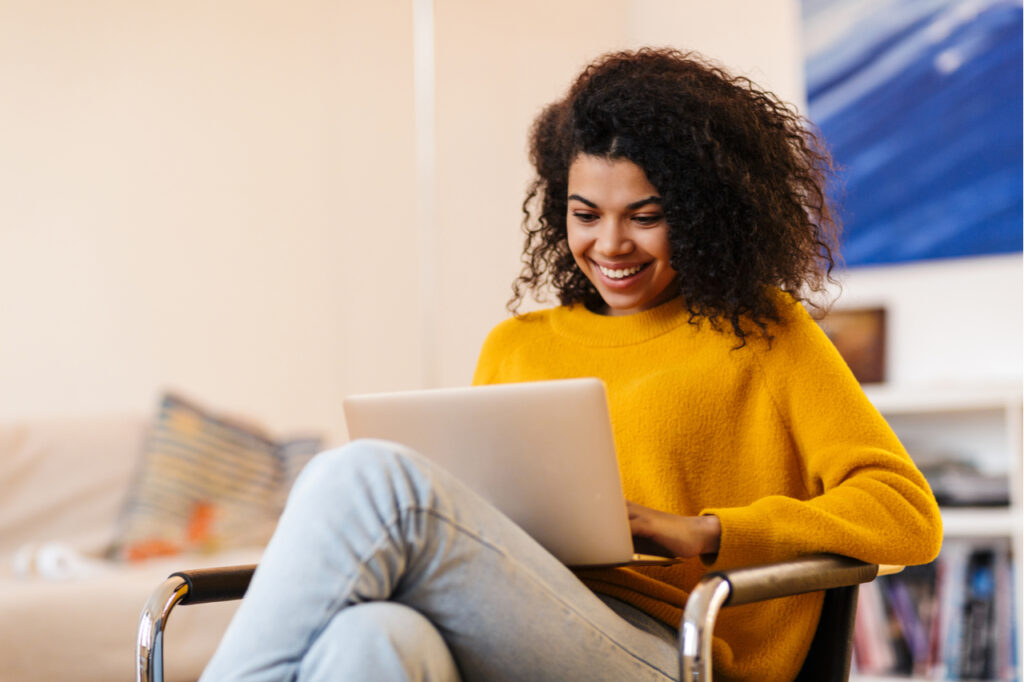 Woman using laptop while sitting on chair in living room.