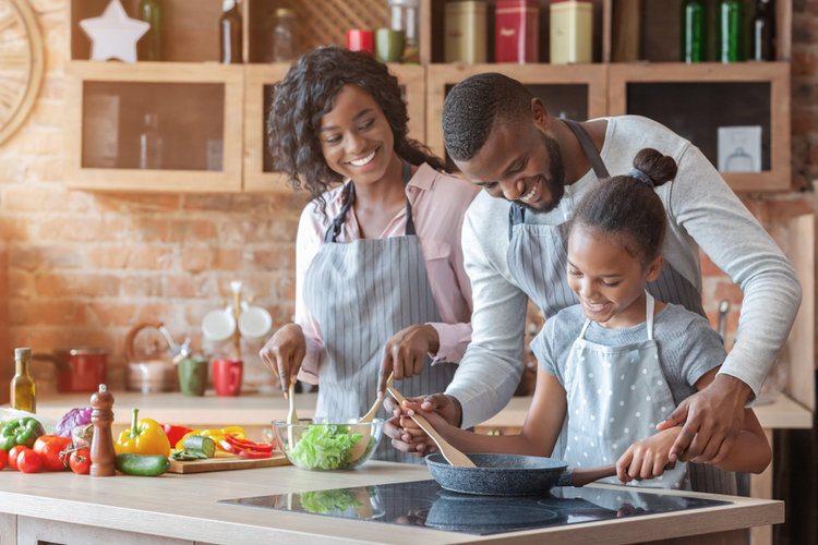 Parents teaching their adorable daughter how to cook healthy food.